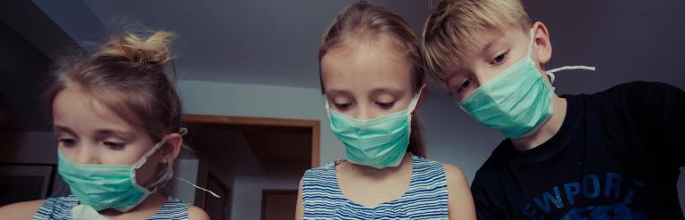 three children wearing surgical masks playing doctors