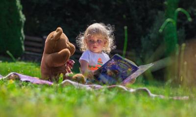 Girl sitting next to a teddy bear reading a book